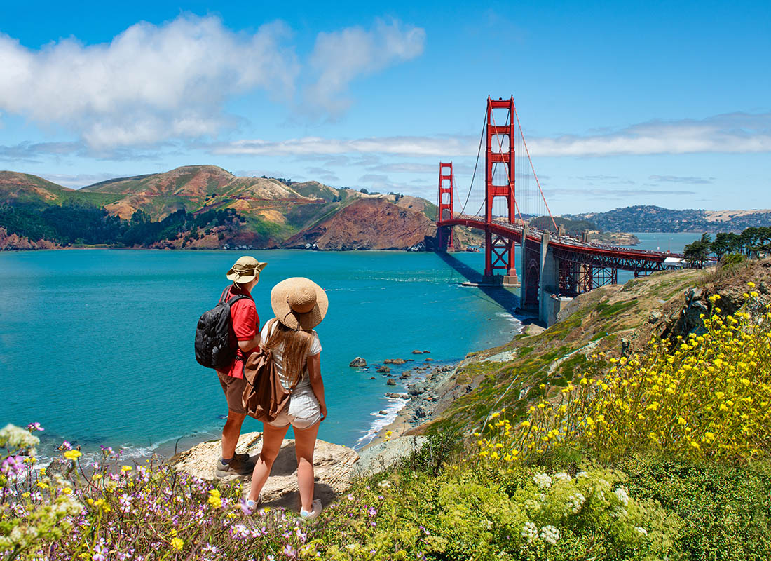 About Our Agency - Couple Standing by a Field of Yellow Flowers Looking at the Golden Gate Bridge